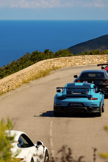 Sports cars driving a coastal road above the sea